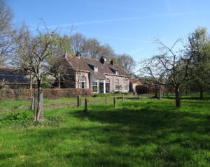 Voormalige stion in Kasteren met op voorgrond groengras en enkele fruitbomen.